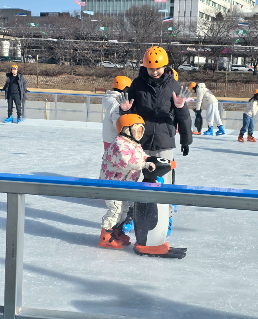 kid holding penguin's hands while skating at a city-run ice rink