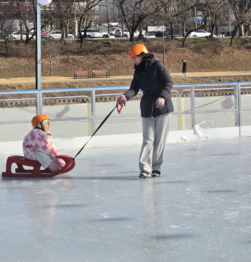 A mother pulling her child on a sled at a winter playground in Korea