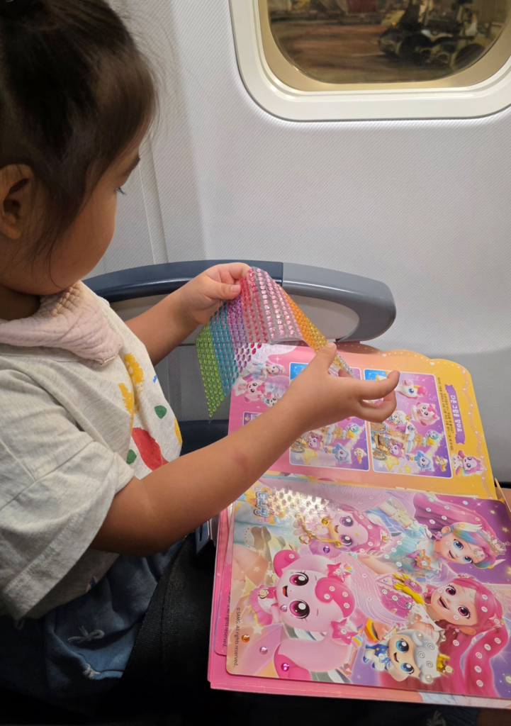 toddler playing with a sticker book on an airplane seat